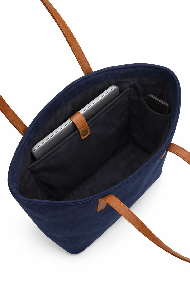 Navy tote bag with brown handles and a compartment containing a laptop and phone on a white background